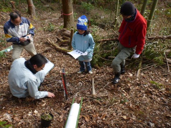 作業着姿の男性が土を触りながら説明をしていて、親子が説明を聞いている写真