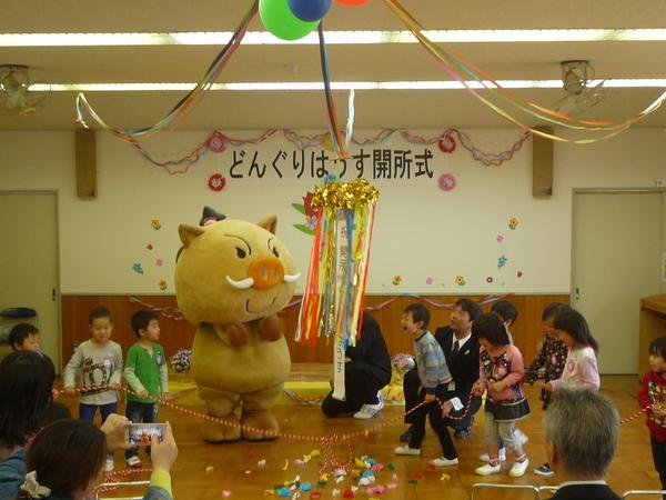 イメージキャラクターの横でくす玉が割れ、子供達が喜んでいる写真