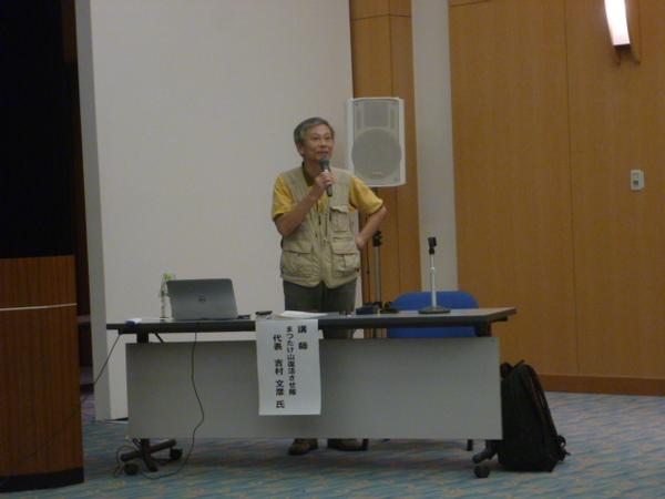吉村 文彦先生がマイクを持ち立って話をしている写真