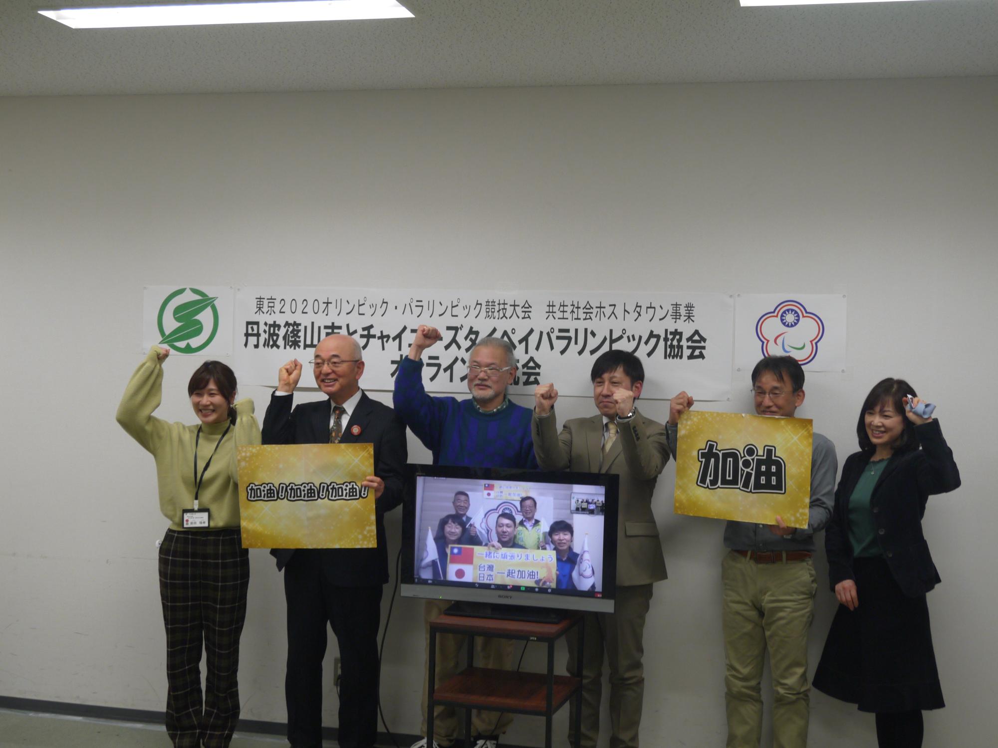 「加油」というボードを持って、市長と卓球協会の皆さんがモニターに向ってガッツポーズをしている。