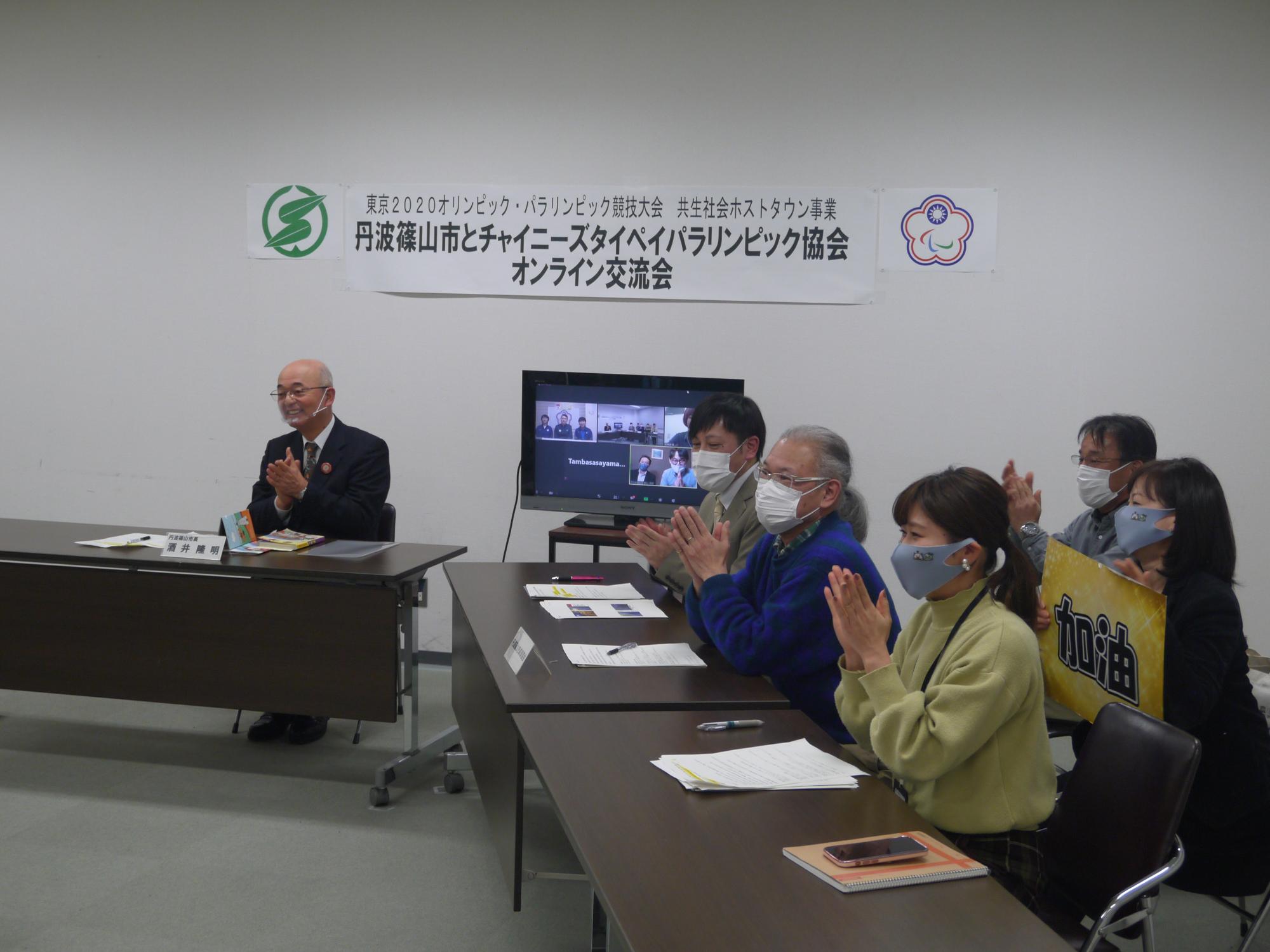 市長と卓球協会の皆さんが椅子に座って拍手している。