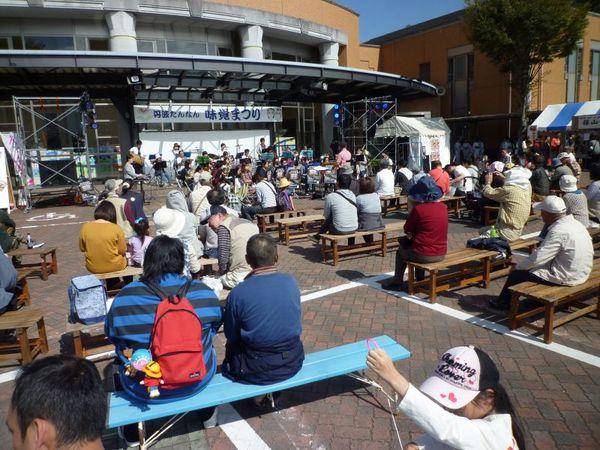 舞台で演奏が始まっているのを観客席から沢山の人が見ている写真