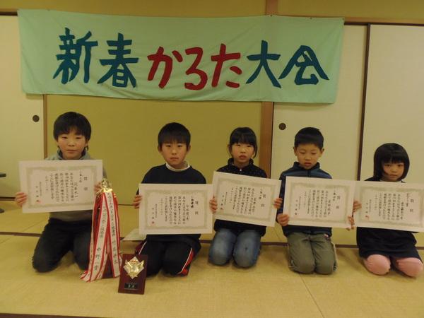 新春かるた大会の横断幕の下に、賞状をもって正座をして並ぶ男女5人の子供の写真