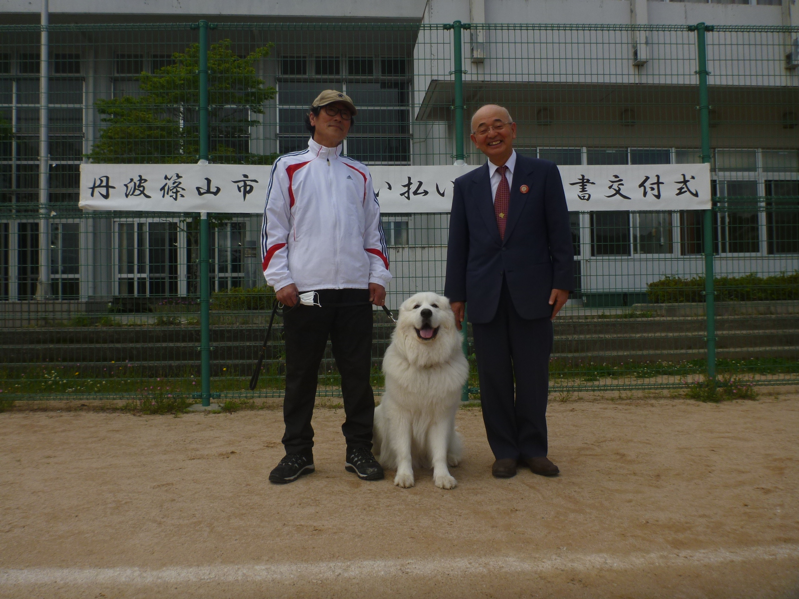 グラウンドで、新しくサル追い払い犬に認定された犬と飼い主、市長の記念撮影。