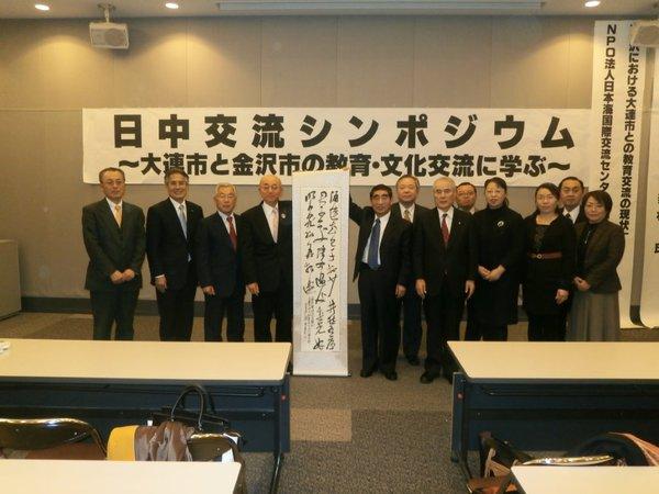 日中交流シンポジウムに参加した方々と中央で市長と関係者の方が草書で書かれた書の掛軸を持って写っている写真