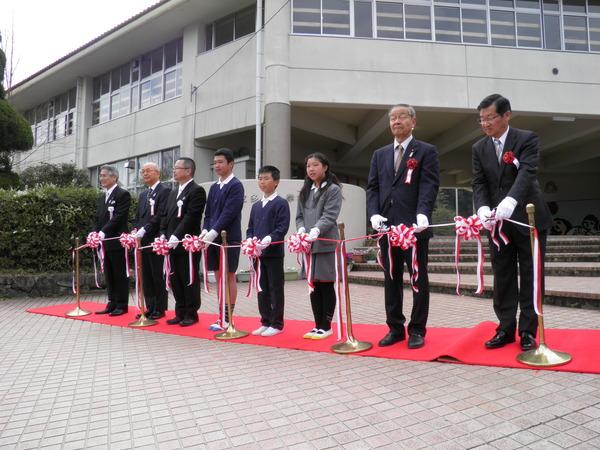 赤い絨毯の上にテープカットのテープがあり、生徒代表3名と市長及び関係者によるテープカットの瞬間の写真