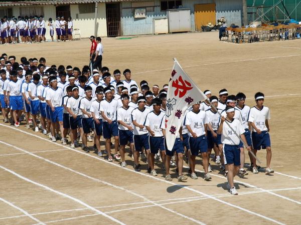 篠山産業高等学校の体育祭の開会式で白色の鉢巻きをして団旗を両手に持った男子を先頭に一斉に行進している写真