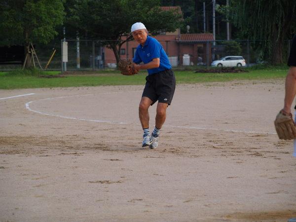 グラウンドで、市長が白い帽子のつばを後にしてかぶり、青いポロシャツと黒い短パンを履いて、左手にグローブを付けて、グローブで掴んでいるボールを右手で掴んで投げようとする直前の写真