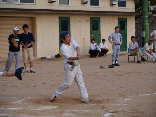 紺色の帽子のつばを後ろにかぶり、白いポロシャツと白いスラックスを着た大上副議長が、バッターボックスに立っており、飛んで来たボールをバットに当てた瞬間の写真