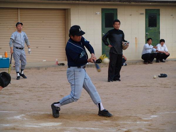 紺色の帽子に、紺色のユニフォームを着ている栗山監督（議員）がバッターボックスに立って、飛んで来たボールをバットに当てる瞬間の写真