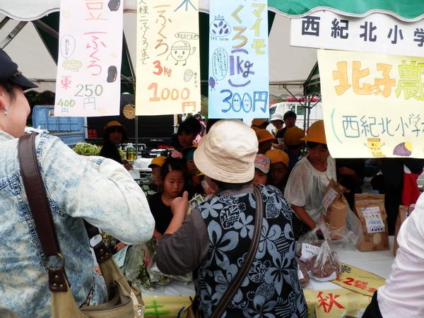 子供達がテントの中で販売してベージュの帽子をかぶったお客さんが支払いをしている写真