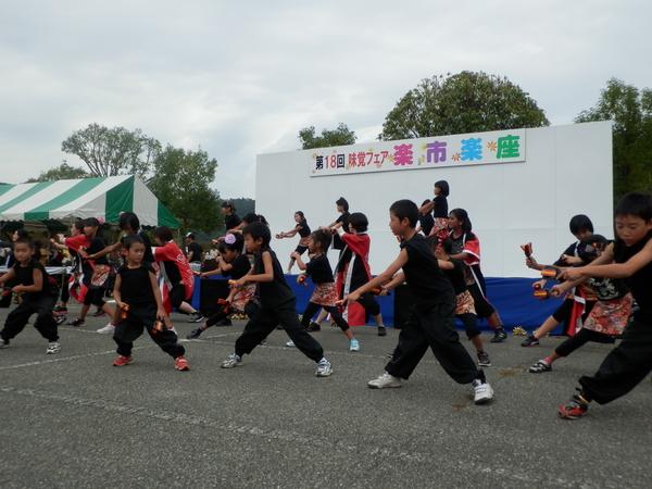 舞台の上と下で黒の衣装でそろえた子供達が元気よく踊っている写真
