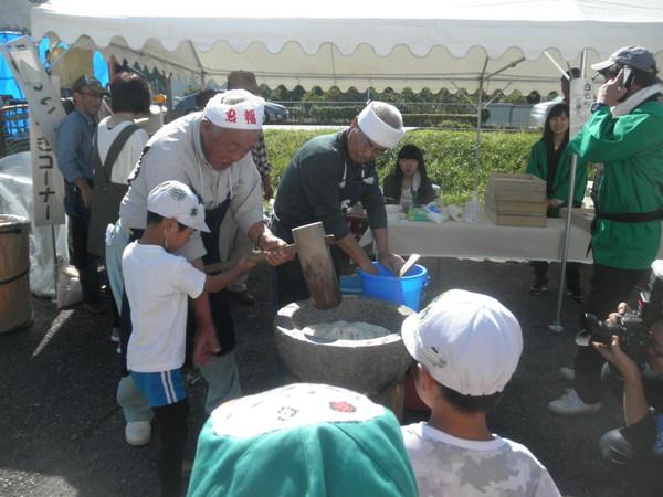 男性が子供に餅つきの仕方を教えている写真