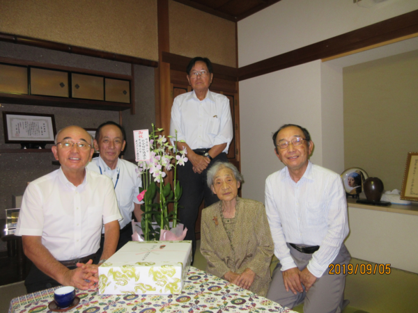 和室で、100歳を超えた女性とお祝いする複数の方々の集合写真
