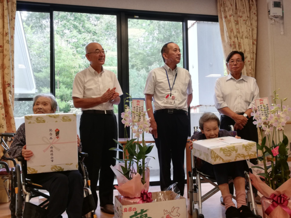 屋内で車いすに座っているご高齢の女性2人と拍手をしている男性達の写真2