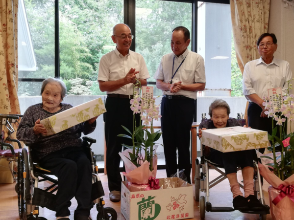 屋内で車いすに座っているご高齢の女性2人と拍手をしている男性達の写真