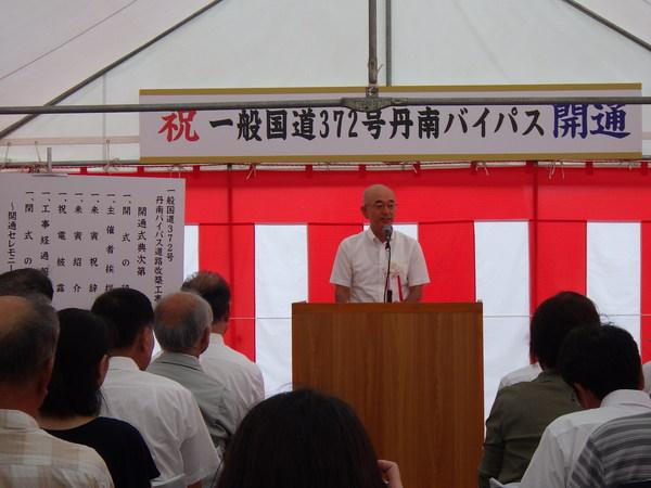 丹南バイパスの開通式にて市長がテントに設置された演壇で話をしているのを聞いている人々の写真