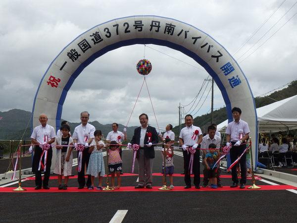 丹南バイパス開通式にて市長や関係者が子供らと一緒にテープカットやくす玉割りをしようとしている写真