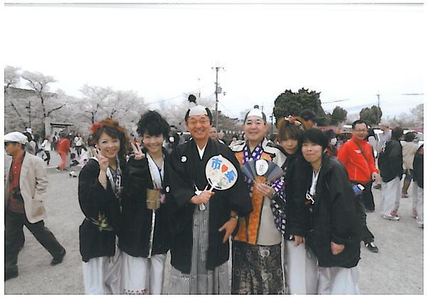 紋付袴を着てちょんまげのカツラを被った市長と議長と白いズボンに黒色の法被を着た女性4人との記念撮影した写真