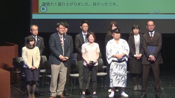 商工観光課チームが発表に望んでおり、舞台上に上がって2列に並んで立っている様子の写真