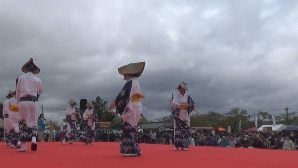 舞台の上で、浴衣のような衣装を着て帽子をかぶって踊る人々の写真