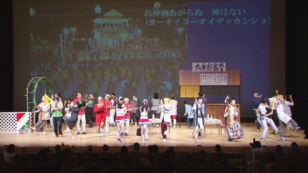 デカンショ踊りの映像がスクリーンに映し出されている舞台で劇に出演した市長らが踊っている写真