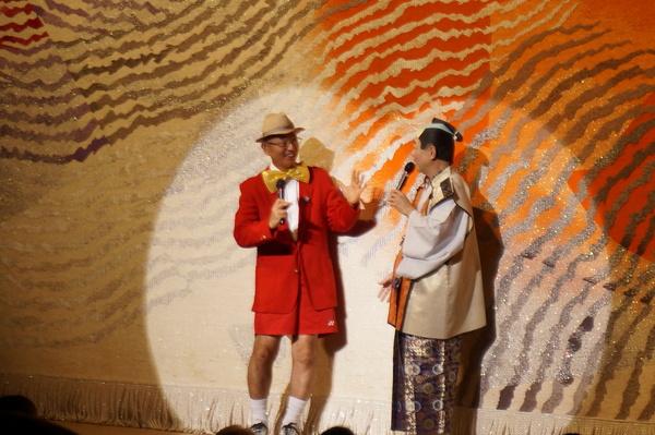 舞台で帽子を被った蝶ネクタイに赤いブレザー姿の市長が殿様と一緒にマイクで話している写真