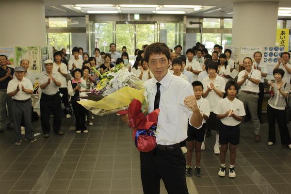 拍手をする参加者のまえで、花束をもってガッツポーズをする角谷 淳志選手の写真