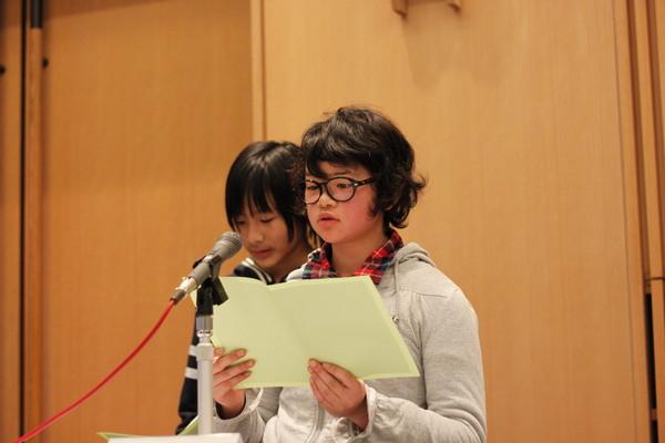 西紀北小学校の女子生徒がプリントを持ち、マイクで発表している写真