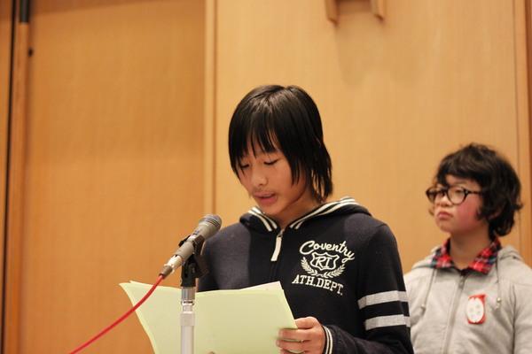 西紀北小学校の男子生徒がプリントを持ち、マイクで発表している写真