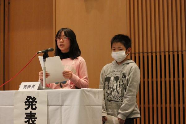 岡野小学校の女子生徒が発表していて隣にマスクをした男の子が緊張してたっている写真