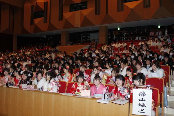 晴れ着姿やスーツ姿の大勢の新成人の方達が座って話をしたり、舞台を見ている写真