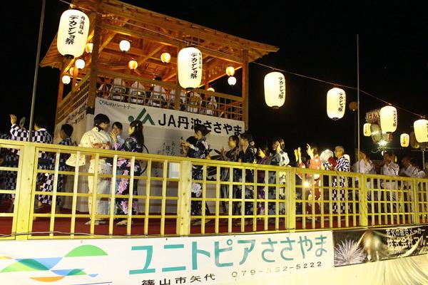 デカンショ祭りと書かれた提灯の明かりが照らされ、その下で浴衣姿で踊っている写真