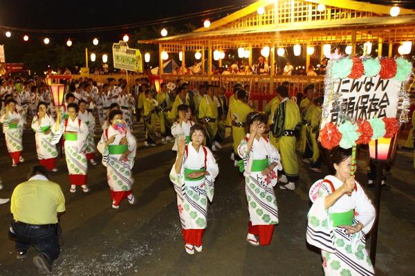 舞台に吊るされた提灯が明るく照らされ色々な浴衣を着た方達が踊っている写真