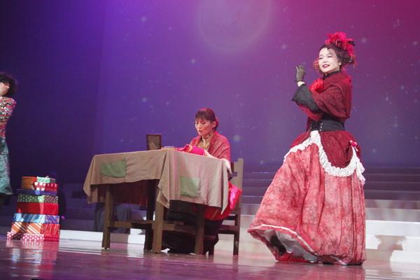 1人の女性は机に座って作業をしておりもう1人の女性は隣で踊っている写真