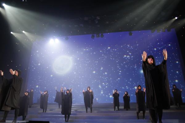 黒い服を着た人たちが手を上げて静かな感じで歌っている写真