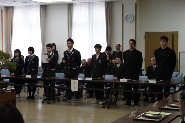 男女の学生が立ち、真ん中の男子生徒が紙を持ち話をしている写真