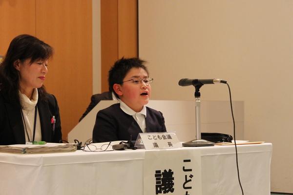 先生が隣に座り、挨拶する小学生の写真