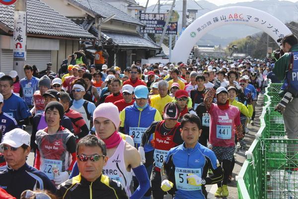 マラソン参加者が道路全体を埋め尽くし走っています。中には知り合いに手を振ったりしている写真