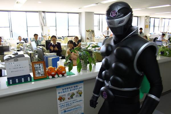 全身黒色の戦闘スーツに身を包んだササグローが市役所に現れ職員が笑顔で出迎えている写真