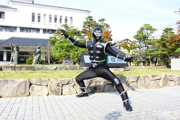 市役所の前で歌舞伎役者のような必殺技のポーズを決めているササグローの写真