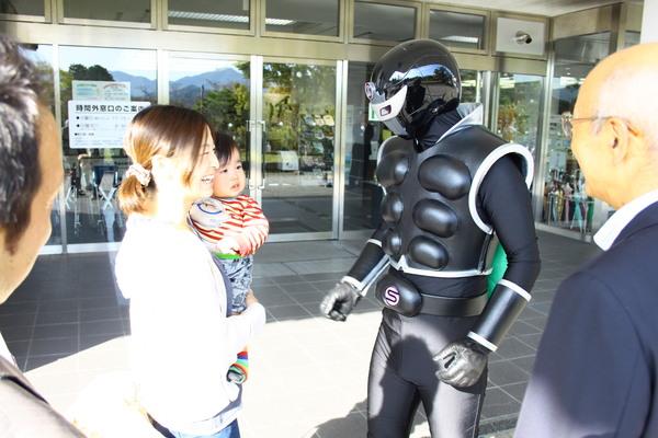 偶然市役所に訪れた母親と赤ちゃんに接しているササグローとそれを見守る市長と職員の写真