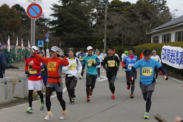 女性ランナーが笑顔で手を上げ、周りの選手もにこやかに走っている写真