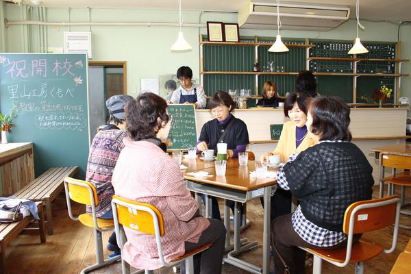 教室が喫茶店となっており、黒板に「祝開校 里山工房くもべ」と書かれ、小学校の机と椅子を使って、お客さんがお茶を飲んでリラックスしている様子の写真