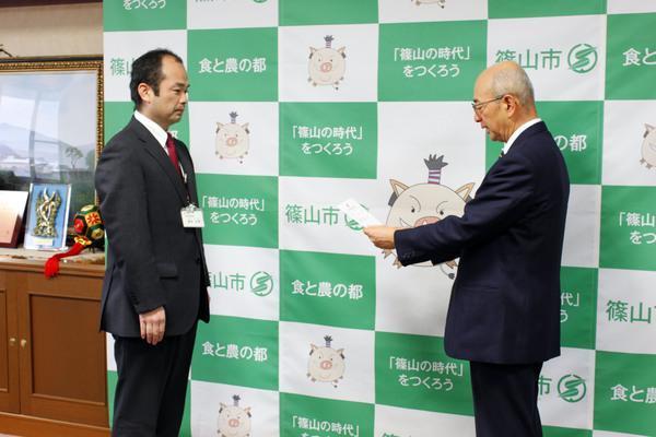 市長室にて、市長より辞令を受けている酒井 正幸さんの写真