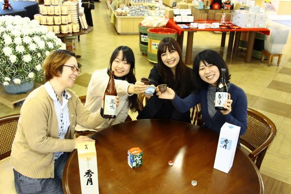 テーブルに座ってお猪口と日本酒を持って笑顔で乾杯している女性4名の写真