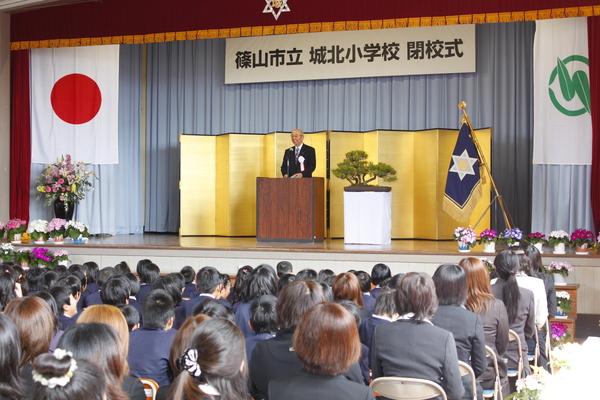 城北小学校のステージ上の演説台の前に市長が立ち、在校生や保護者に話をしている写真
