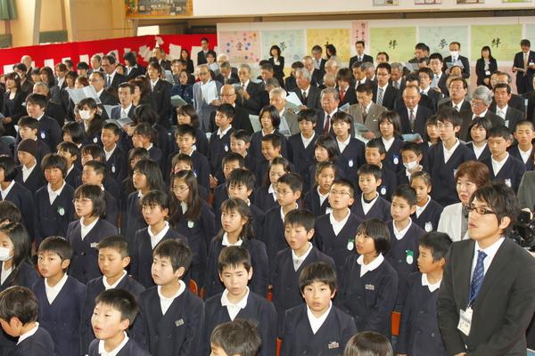 在校生、保護者、先生方などその場で起立し、歌を歌っている写真