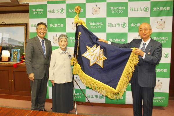 城北畑小学校の校旗を持つ市長と、その横に立つ年配の女性と、男性の写真