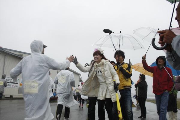 かつみさゆりさんが走ってくるカッパを着た選手にハイタッチしている写真